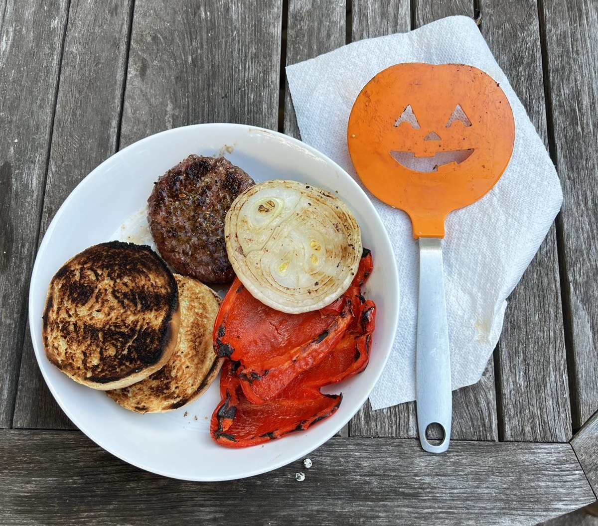 A solo backyard dinner plate with a burger, grilled onion, and roasted pepper.